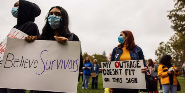 Image shows to two women holding signs saying "Believe Survivors" and "My Outrage Doesn't Fit On This Sign"
